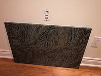 Full view of granite stone slab leaning against wall with measurement label visible.