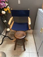 Both the folding directors chair and the wooden stool placed on tiled flooring, showing front view of the chair and top view of the stool.