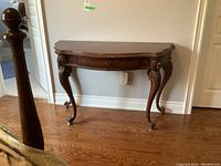 Full view of dark wooden hall or console table with curved legs and scratched surface.