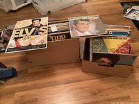 Photo showing multiple vintage vinyl albums stacked in cardboard boxes, prominently featuring Elvis Presley and Dean Martin albums.
