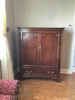Front view of Strathroy wardrobe cabinet showing two paneled doors with carved corner accents and brass handles, plus bottom drawer with brass handles.