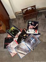Photo showing the wood magazine rack in upright position with multiple vinyl record albums scattered in front, clearly showing recognizable album covers from U2, The Beatles, Steve Miller Band, and others.