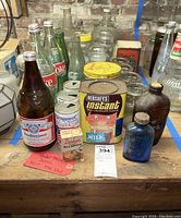Overview of collection showing beverage bottles, tins and jars including prominent Budweiser bottle and Hershey's Instant cocoa tin.