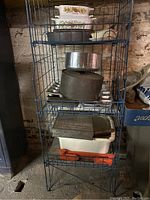 Full view of cookware and wire shelf with multiple pans and dishes stacked on it in a rustic setting