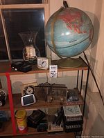 Photo of a 12-inch globe on metal stand with vintage alarm clocks and radios on shelf beneath it.