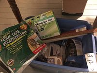 Blue bin with multiple window repair items including foam tape weatherstripping, window insulator kit box, deadbolt handles, and a wooden ruler.
