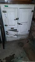 Front view of vintage white wooden icebox with two large doors and one smaller bottom door, showing wear, paint chips, and rusted metal hinges and latches.