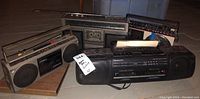 Photo showing four portable radios/boomboxes arranged with visible brand logos and features