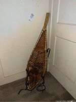 Full view of both snowshoes leaning against a wall showing the metal frame and wooden lattice decking with attached bindings.