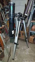 Full view of the black Infinity AA4EQ telescope mounted on a silver aluminum tripod stand in storage environment