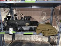 Black plastic train model labeled 'Pioneer 49', showing front side with wheels and funnel, placed on a metal shelf with a folded green blanket and warmer next to it.