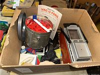 Overall view of the Vac-U-Form set in cardboard box showing a metal bucket containing red plastic American brick molding pieces, the Vac-U-Form machine, and other parts with the instruction booklet visible.