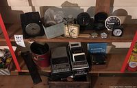 Overview of multiple clocks, cassette recorders, portable radios on shelves including small and larger clock faces, showing wear and dust.