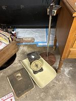 Photo showing vintage metal food scale with dial on flat pan, black textured step on scale, and metal detector stand with detection device attached.