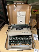 Smith-Corona typewriter inside beige hard carry case with instruction booklet propped inside lid.