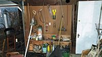 Wide view of yard tools and assorted items hanging on pegboard and placed on shelves including sprayers, rakes, saws, and containers.