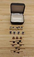 Photo of multiple men's formal shirt studs and clips displayed in front of a small black jewelry box with white interior.