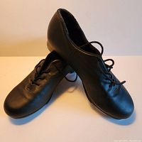 Front angled view of pair of black Capezio tap shoes showing leather upper and lace-up design.