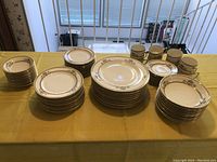 Full spread showing the complete china set including stacks of plates and arranged cups with saucers on a yellow tablecloth.