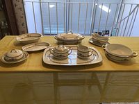 Full view of the 9-piece vintage Noritake china set displayed on a yellow tablecloth showing bowls, platters, tray, gravy boat, creamer, and sugar bowl with lids and gold floral trim.