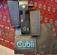 Top view of Cubii elliptical exerciser on top of branded exercise mat, showcasing foot pedals and central console.