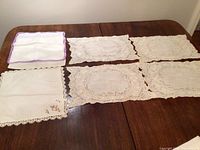 Top view of various lace placemats and embroidered napkins laid on a wooden table.