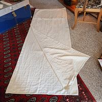 Full view of cream colored duvet cover laid out on a red patterned carpet showing slight folds and a quilted pattern.