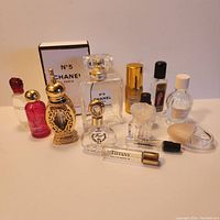 Photo showing 11 empty vintage and used perfume flacons in various designs and brands, including Chanel No. 5 with box and Tiffany Eau de Parfum, arranged on a white surface.