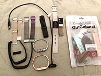 Multiple Fitbit trackers, charging cord, and replacement bands displayed together on a beige surface.