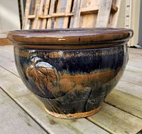 Side angle view of glazed ceramic garden pot showing blue glaze and raised golden leaf motif with wear and minor chipping at rim and base.