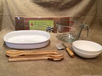 Photo showing all items including the white ceramic casserole dish, Pyrex measuring cup, wooden spoon and spatula, vegetable crinkle cutter, Fitz & Floyd bowls, and grilling planks.