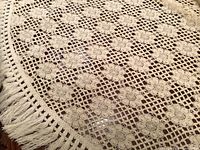Full view of the large ecru lace bedspread showing floral crochet pattern and fringe on one edge.