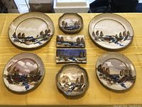 Top view of 8 pottery pieces laid out on table showing hand-painted abstract designs in brown and blue on light tan background.