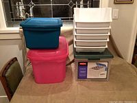 Photo showing pink large bin on bottom, blue bin on top, stacked white bins and green base with boxed item underneath.