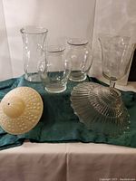 View of assorted clear glass vases and two decorative glass dishes on a fabric surface