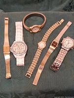 Photo showing six assorted watches laid out on a dark fabric surface for overview.