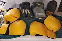 Three pairs of boxing mitts including two yellow pairs and one Everlast grey pair displayed on towel.