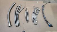 Multiple braided metal hoses grouped by size and fitting type laid out on floor.