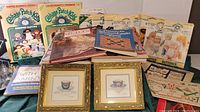 Photo showing lot of assorted Cabbage Patch Kid sewing pattern booklets, sewing and craft books, and two framed tea cup photos with gold frames.