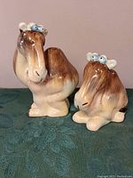 Front and side view of the two camel salt and pepper shakers, showing their shape and colors on a textured green surface.