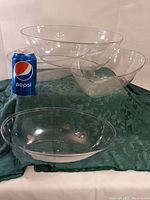 Three clear oval plastic bowls displayed on a green cloth with a Pepsi can for size reference.