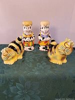 Front view of both sets of cat-themed salt and pepper shakers showing color and design details of each pair.