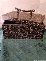 Black rectangular box with gold circle pattern and removable lid with gold-colored handle