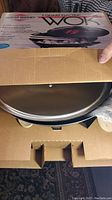 Electric Wok inside original box, showing packaging and unopened wok with wooden spatula and handles visible.