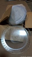 Photo of multiple clear plastic platters stacked inside an open cardboard box showing the radial spoke pattern and ridged rim detail.