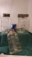 Three large glass jars displayed with a can for scale, two standing and one lying down, all having metal lids.