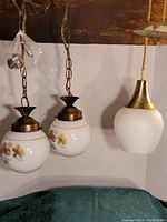 Front view of three MCM hanging lights showing two floral double globes on chains and one single smooth white globe with brass fittings