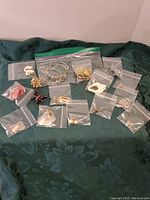 Various jewelry pieces including earrings and bracelets displayed on green fabric, all individually bagged.
