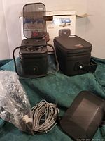Photo of two black Pyramid mini monitor speakers with metal grilles, cables, plastic wrapping, carrying case, and product box in background.