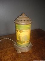 View of assembled antique brass lamp with painted panoramic landscape of Niagara Falls on a cylindrical shade, brass ornate perforated top and base, electric cord attached.